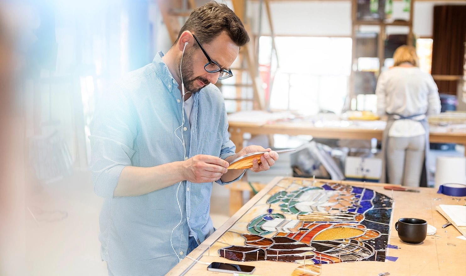 A glassworker is listening to music in headphones as her works on a stained glass piece in a shared studio.