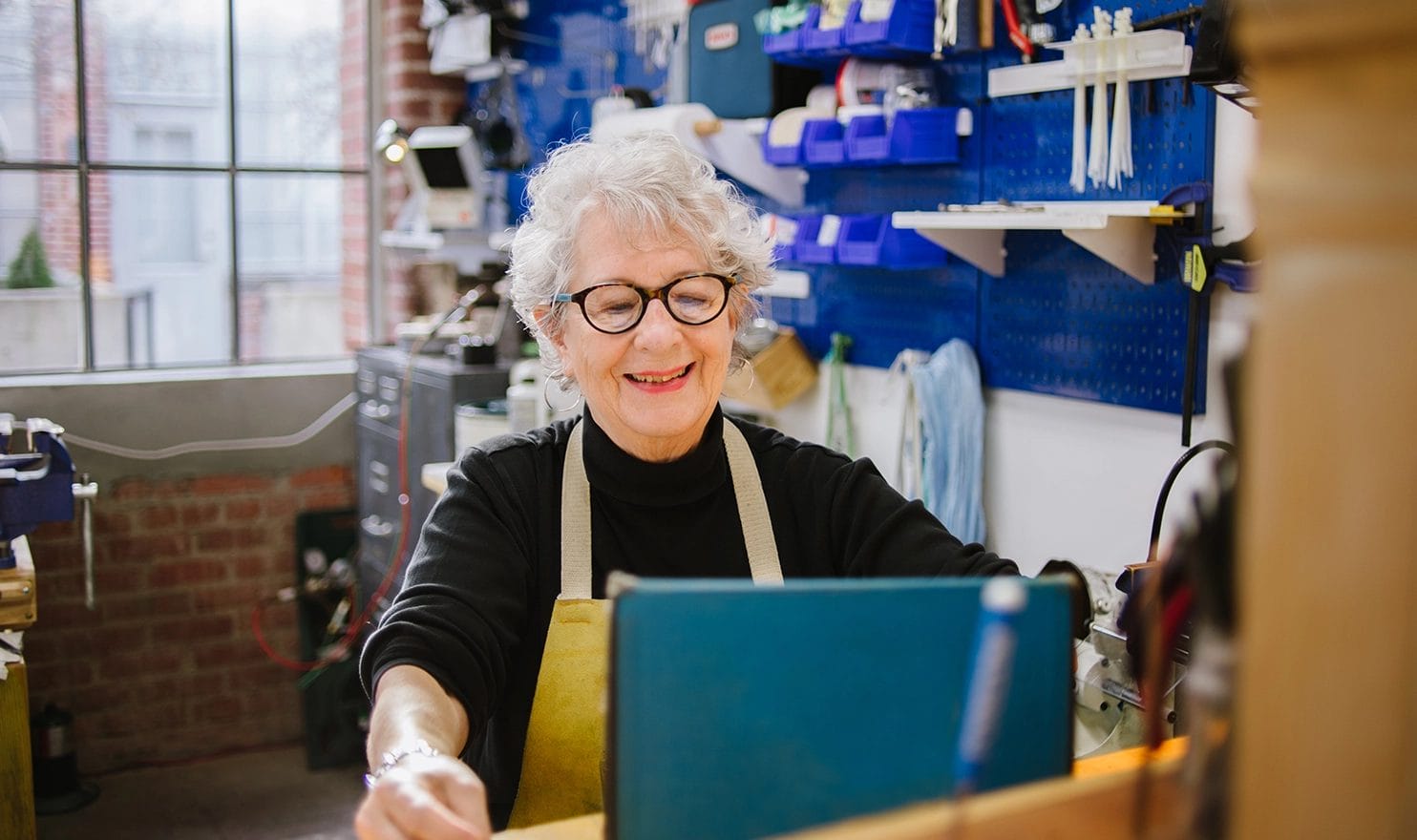A female creative is happily smiling at her laptop as she responds to customers online from her studio.
