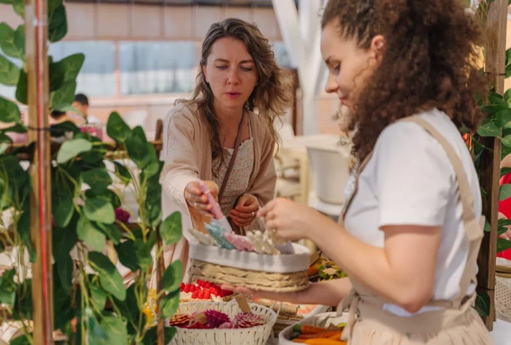 a craft fair vendor helping a customer choose candles