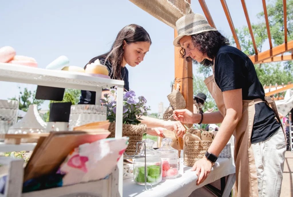 a soap vendor helping a customer at an outdoor market in summer