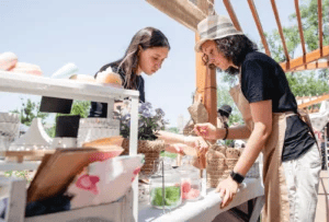 a soap vendor helping a customer at an outdoor market in summer