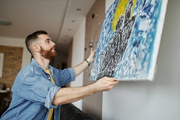 A man hangs a custom painting on his wall in his living room.