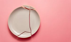 A broken clay plate on a light pink background.
