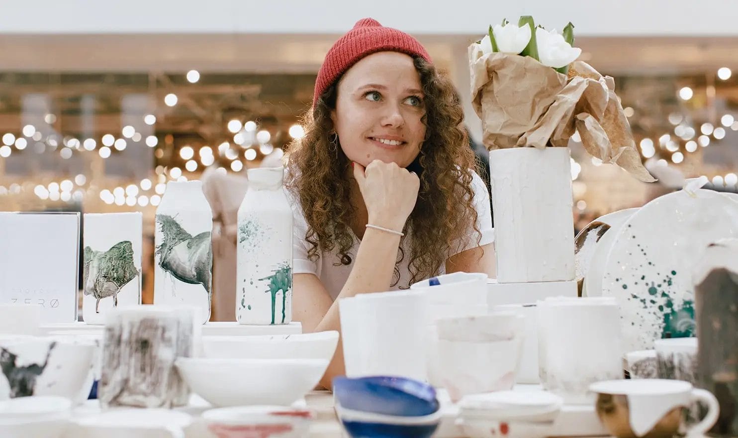 A vendor is smiling at her booth as she looks around at the craft show and waits for the chance to sell her handmade pottery.