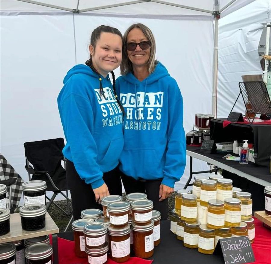 A pair of vendors at the Ocean Shores City Market happily posing for a photo next to their homemade jams displayed in their booth.