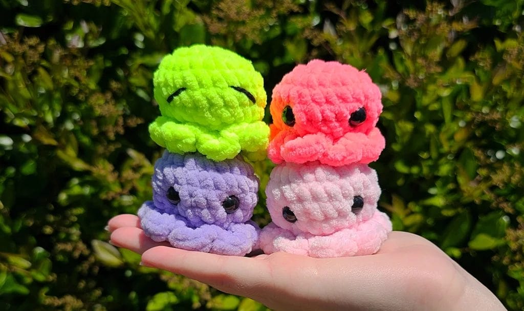 Colorful crocheted amigurumi octopi posed on an artist's hand for a close-up photo.