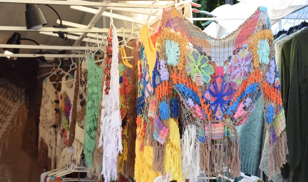 Close-up knitted clothes in crochet style, hanging on a rack at an outdoor craft fair.