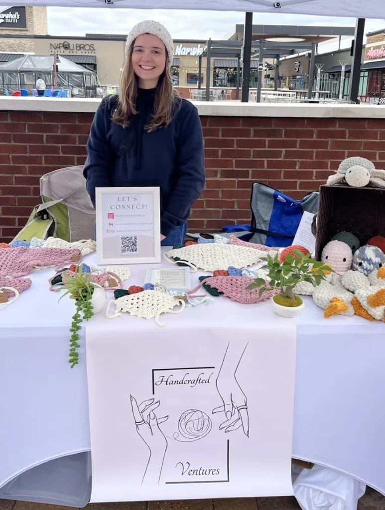Abby smiling behind her booth as she sells her crocheted crafts at an outdoor market.