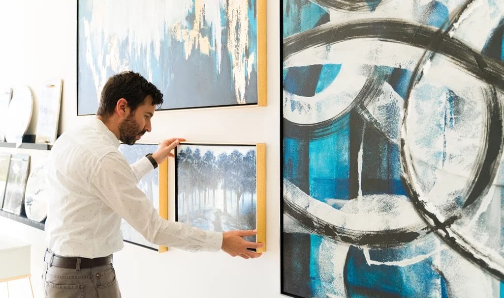 Male artist fixing his small painting hanging on the wall at an art exhibition.