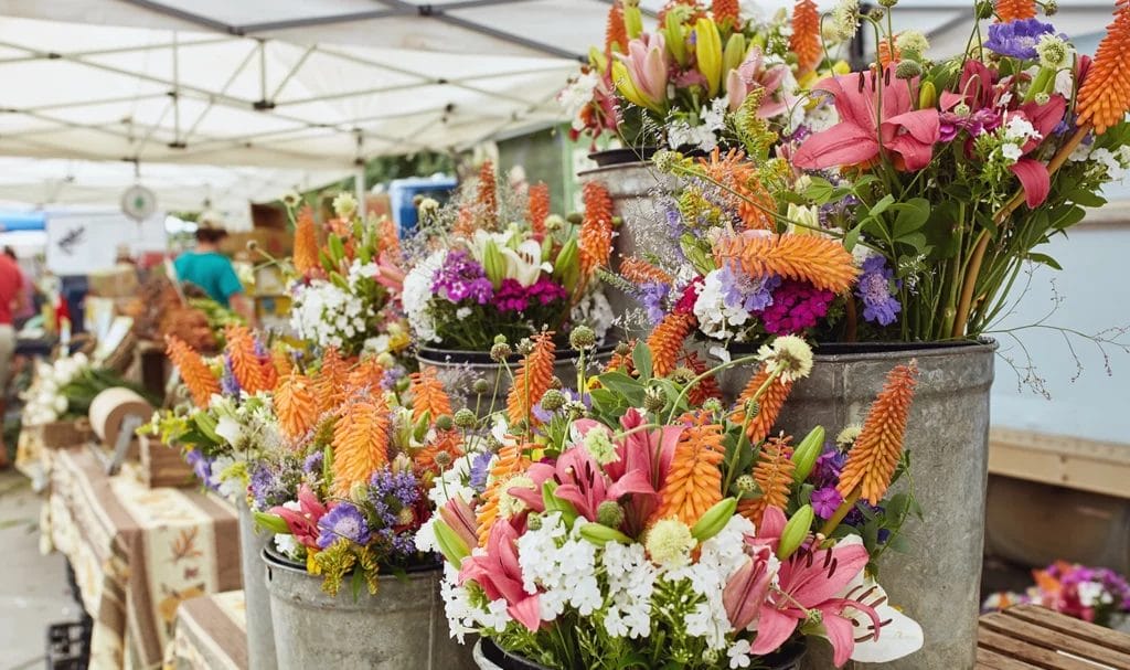 Bouquets of fresh-cut flowers on display in metal buckets in a vendor's booth at an outdoor farmers market.