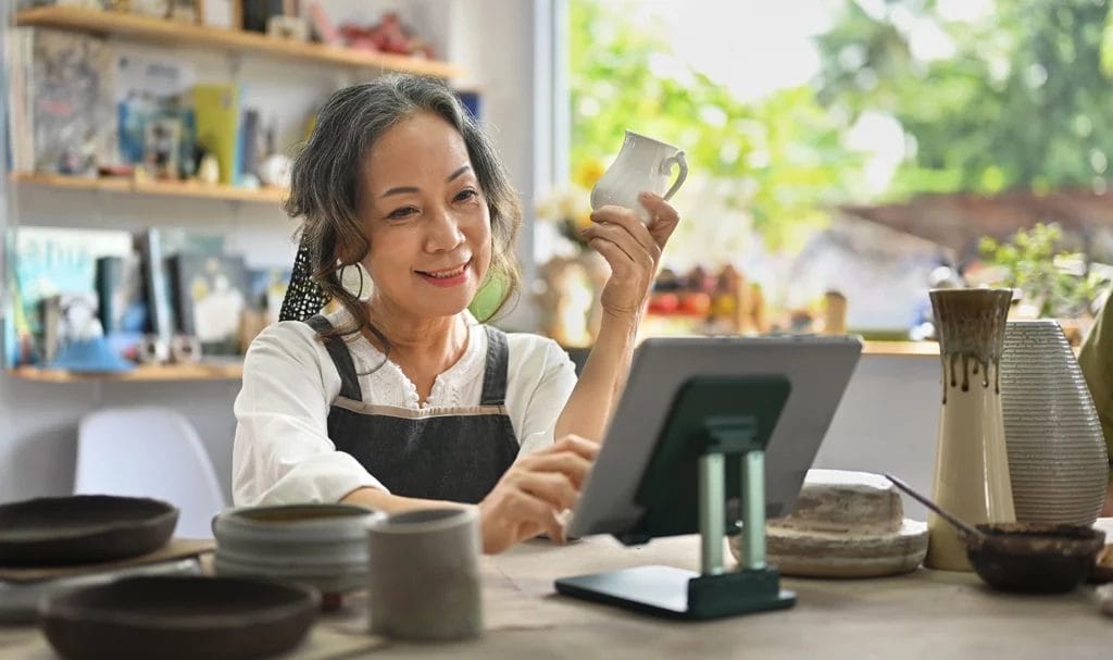 Senior craftswoman with tablet computer in earthenware studio.