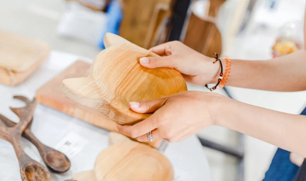 A customer holds a handmade wooden board for sale at a booth in an outdoor market.