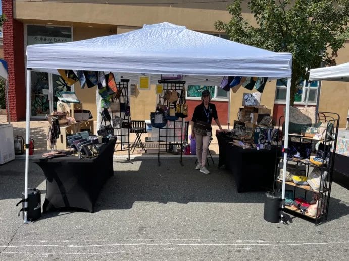 Linda R posing with her booth display at a local craft fair.