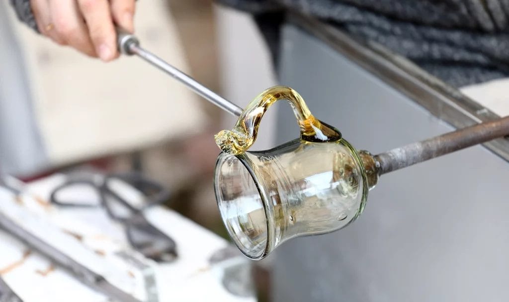 An artisan carefully placing and shaping the handle on a glass cup.