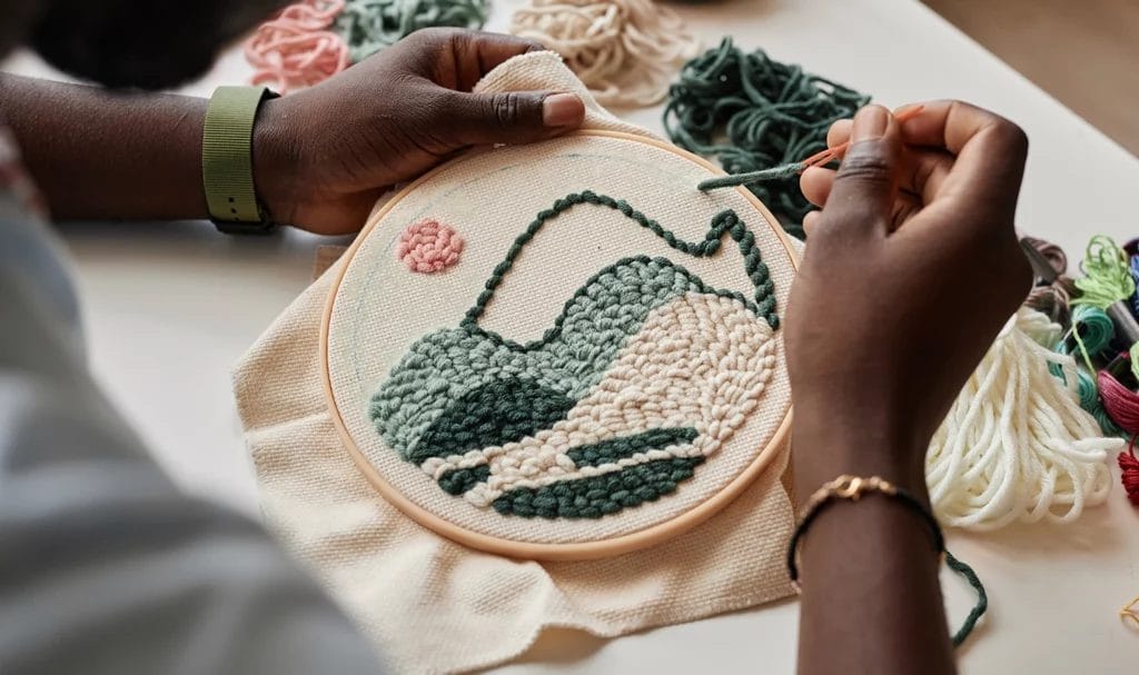 Close-up look of an artisan creating a landscaped embroidery scene on a piece of white canvas with a circle hoop.