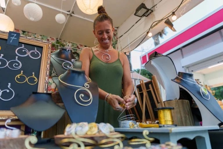 a female artisan creating metal wire jewelry inside a booth at an outdoor art market