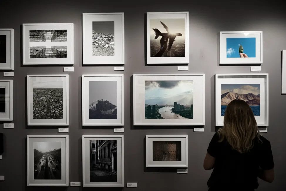 A woman looks at a gray wall at an art show covered with photography pieces in white frames.