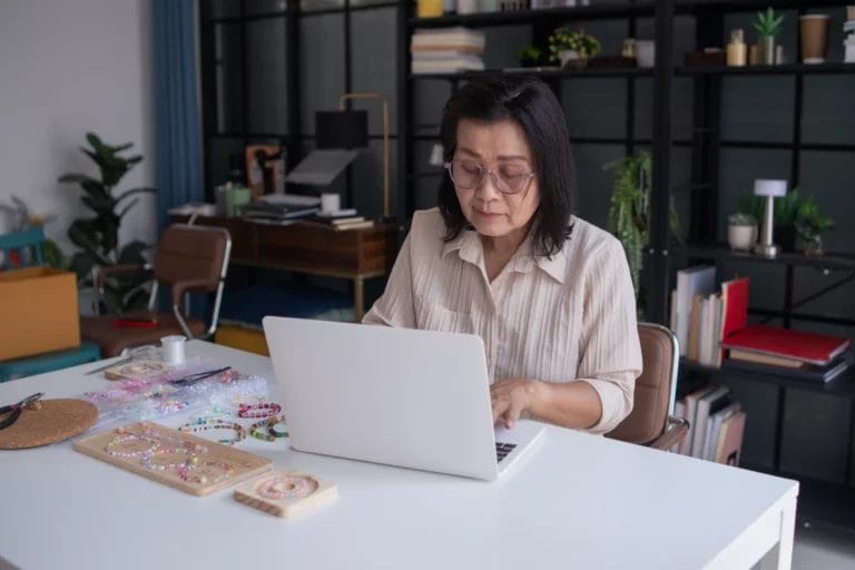 a handmade jewelry maker using a laptop inside her office