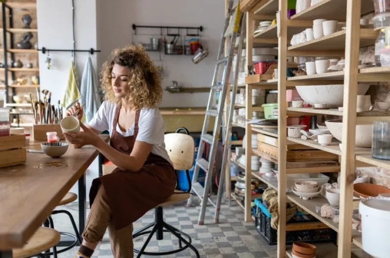 a pottery artist painting a bowl while seated in an art studio