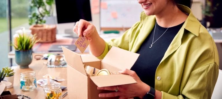 a close up of a female craft business owner placing handmade items into a box with a thank you note