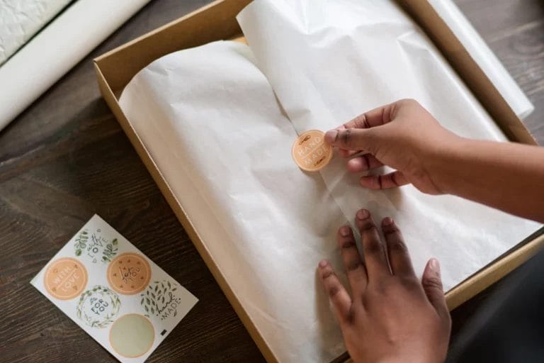 a woman placing a sticker saying handmade on top of wrapping paper inside a package