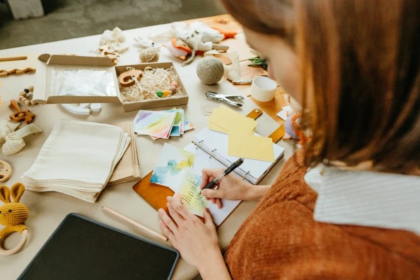 a young woman writing a thank you card next to miscellaneous craft packaging items