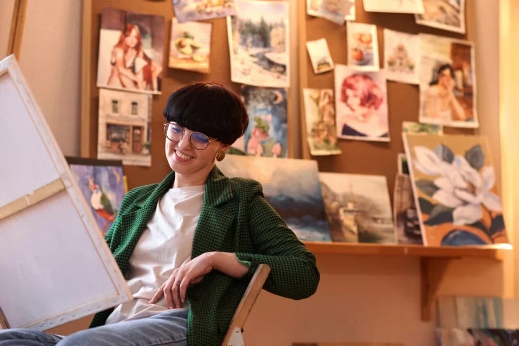 a young female artist smiling while looking at a finished painting in an art studio