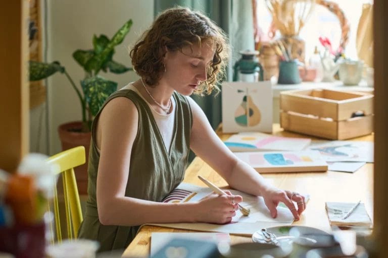a young woman painting abstract artwork while seated at a desk