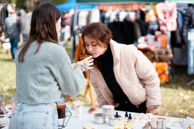 handmade candle vendor letting a customer smell a scented candle at an outdoor market