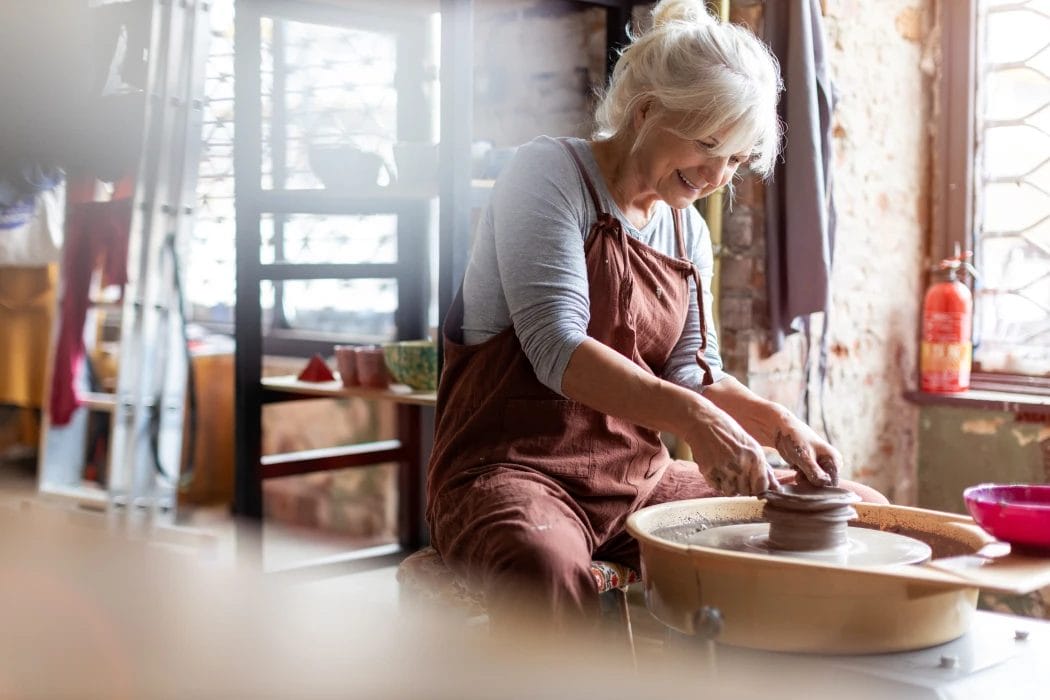 a senior woman smiling while shaping clay on a potters wheel