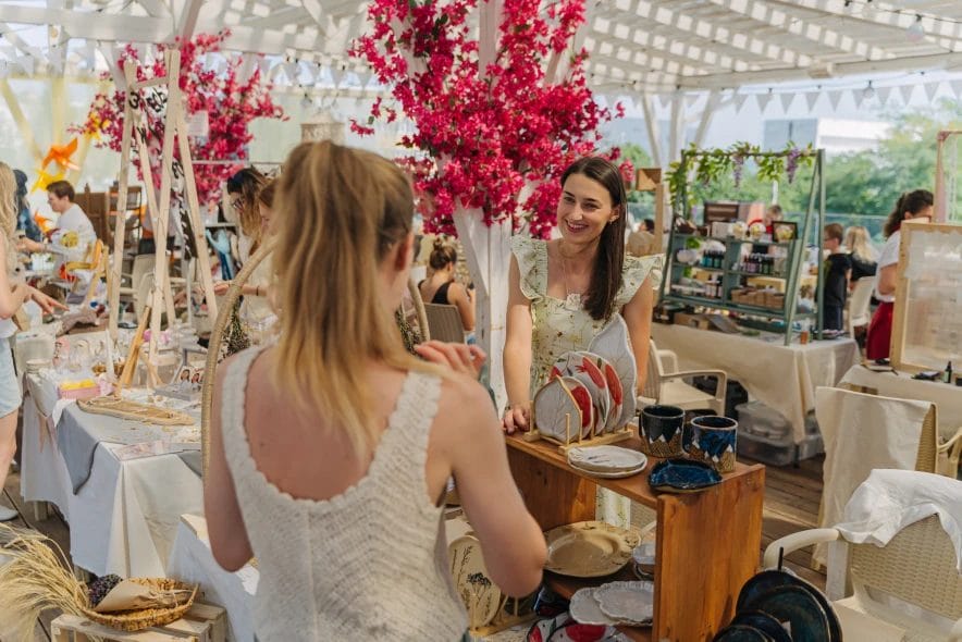 a pottery vendor talking to a customer while at her booth at an outdoor market