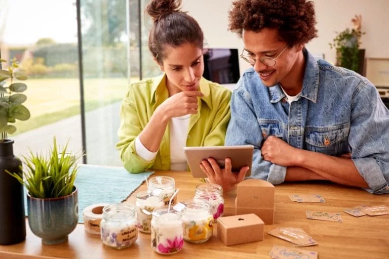 a couple running an online candle business looking at a tablet surrounded by candles and labels